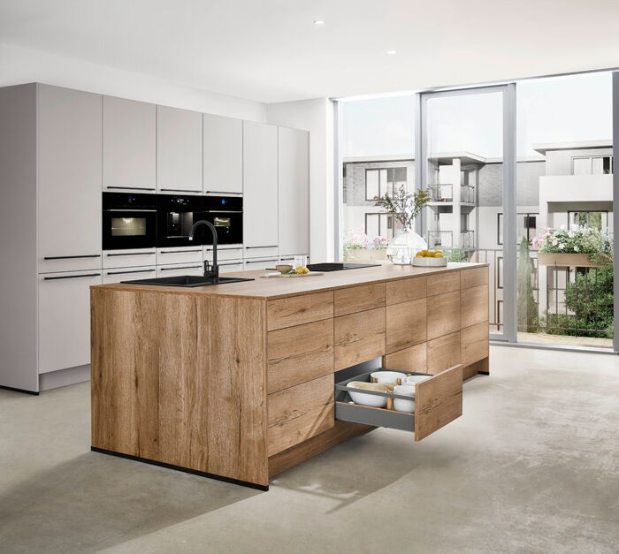 Zeitgemäße Küche mit Holzfronten und offener Schublade, Blick auf Balkon und Wohngebäude.