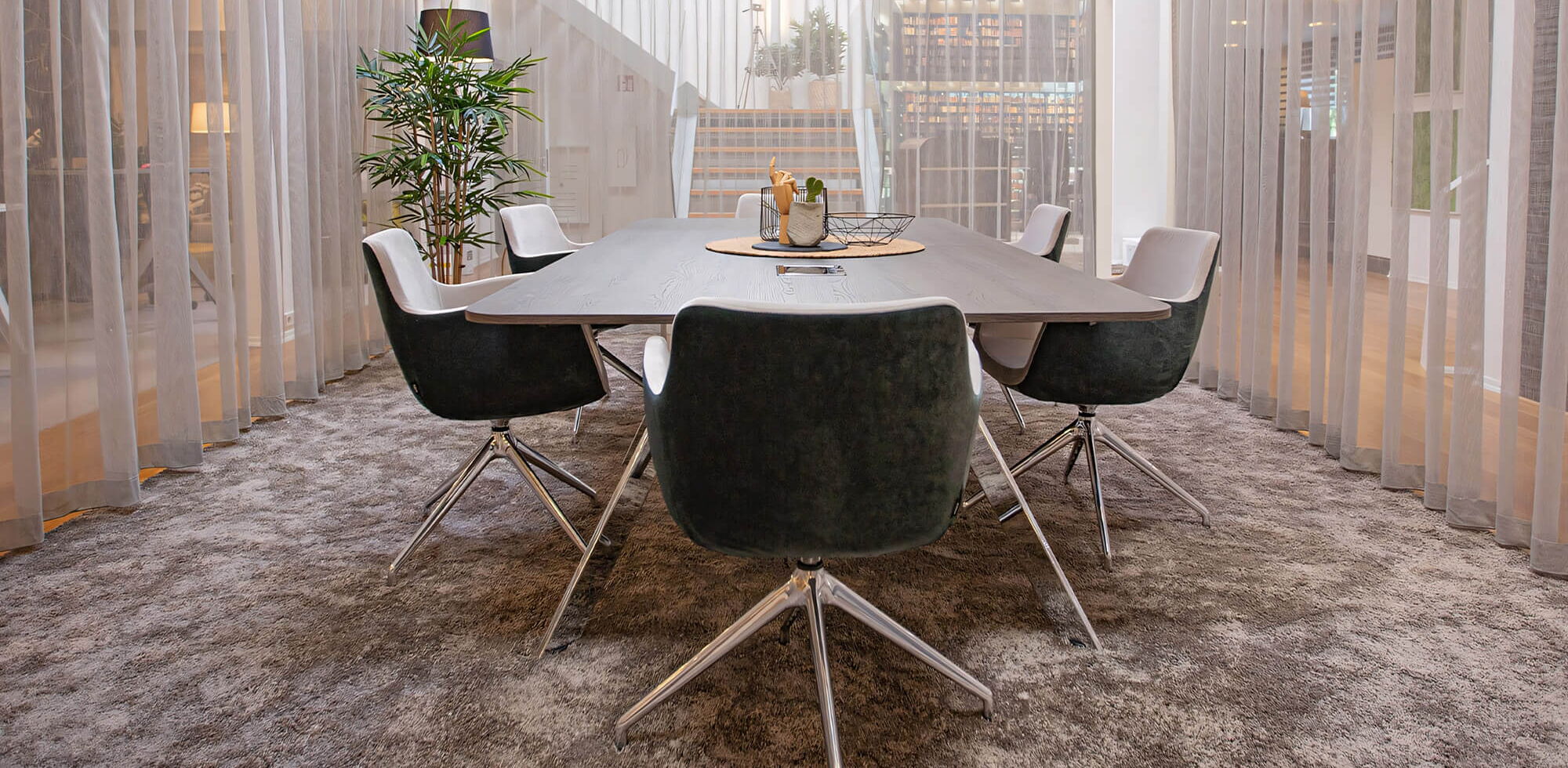 In einem offenen Bürogebäude ist der zentrale Meetingbereich mit großem Tisch mit halbdurchsichtigen Vorhängen abgetrennt