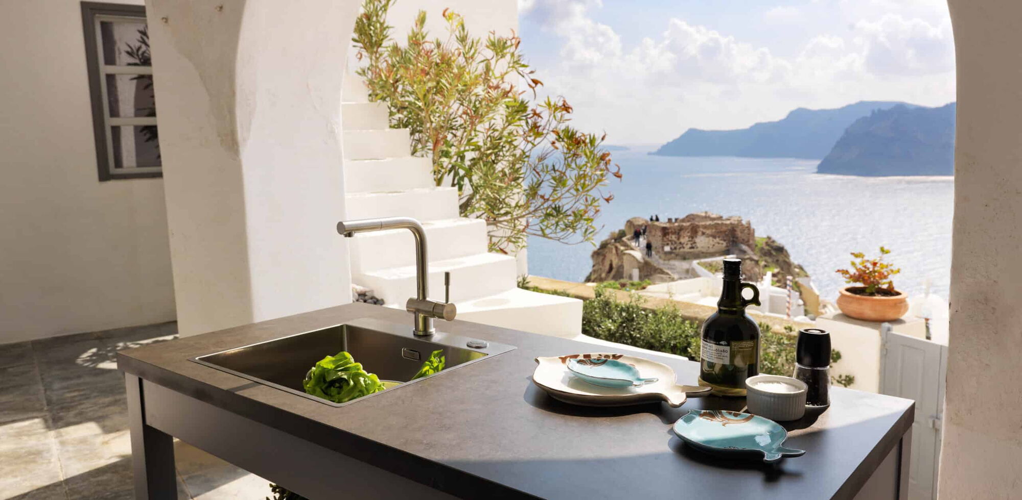 Tisch mit integrierter Spüle und Geschirr, Blick auf das Meer und eine mediterrane Landschaft.