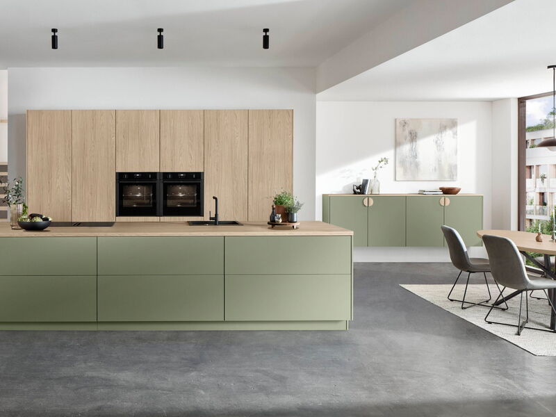 Eine grüne Küchenzeile mit freistehendem Block inkl. Herd und Spüle in einem modernen, lichtdurchfluteten, offenen Raum