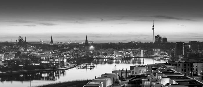 Ansicht der Skyline von Dortmund bei Dämmerung mit Wasserfläche, Gebäuden und Fernsehturm im Hintergrund.