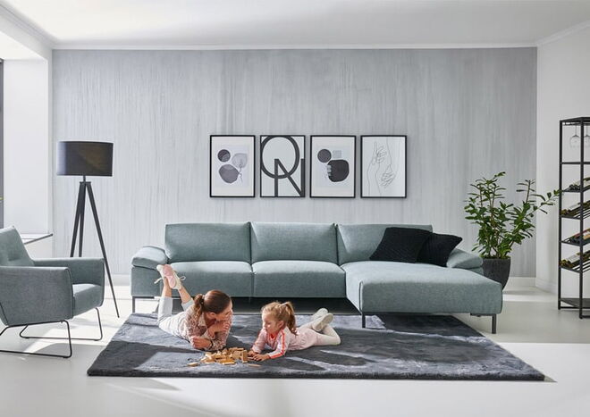 Vor einer grauen Couch spielt ein Kind mit seiner Mutter