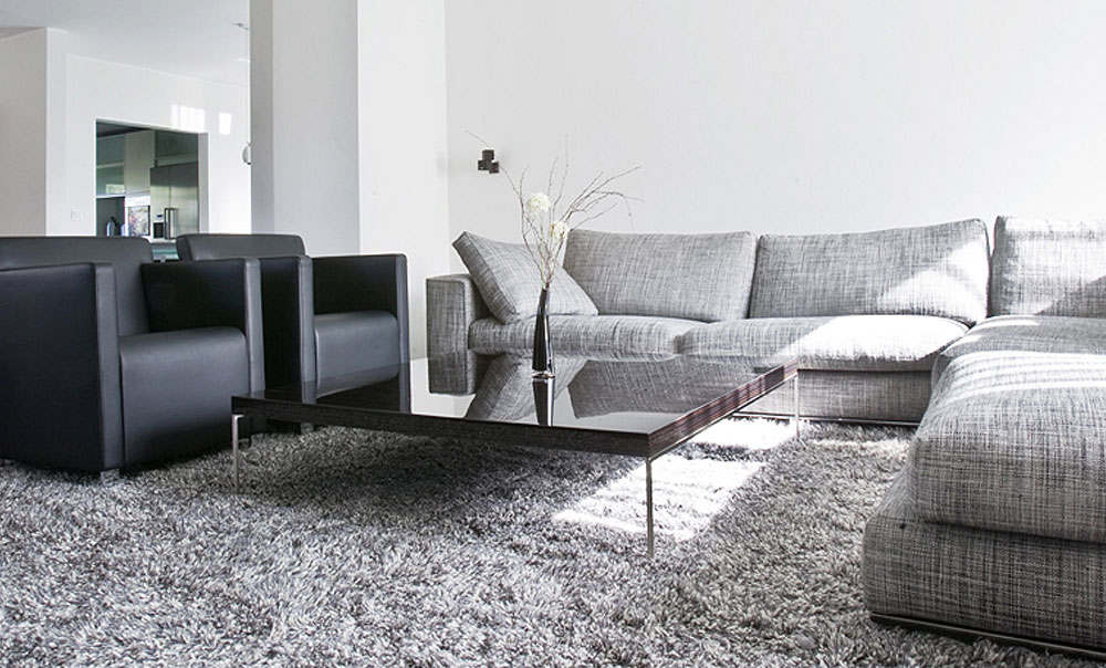 Hellgraue Couch und schwarze Ledersessel in einem Wohnzimmer